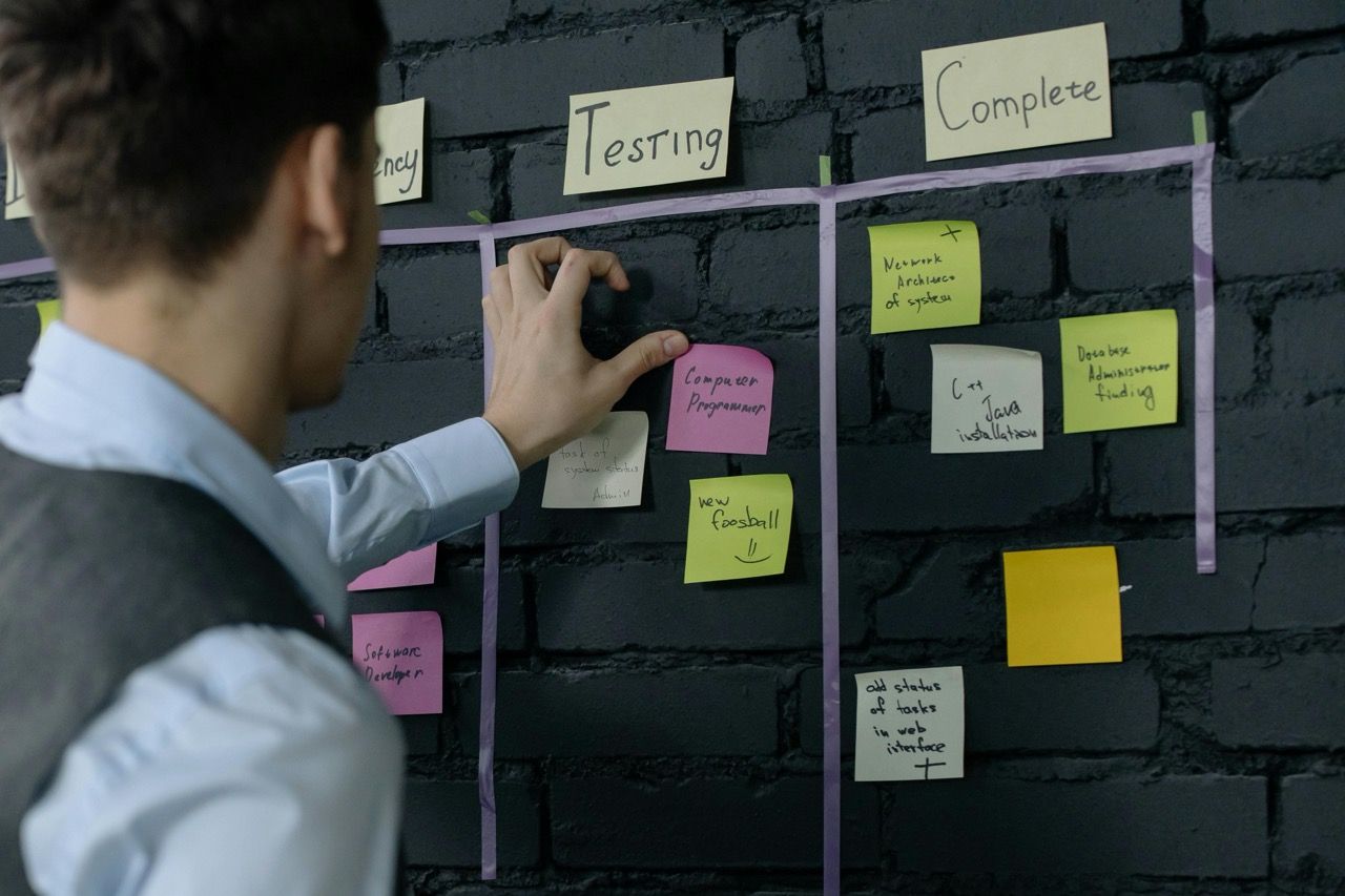 Person uses a Kanban board with sticky notes to visualize a workflow with phases such as “Testing” and “Complete”.