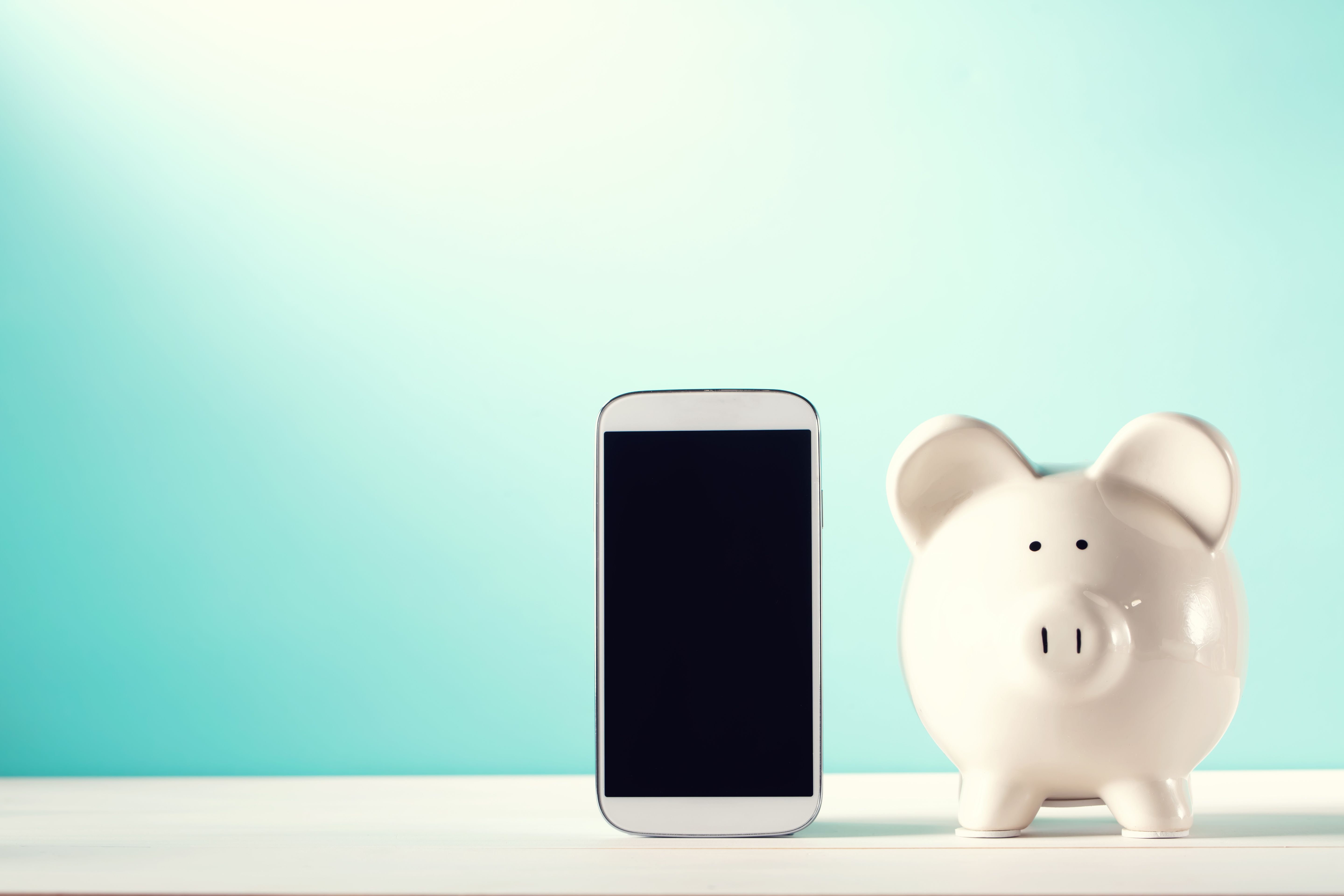 A piggy bank is on a table to the right of an upright smartphone.