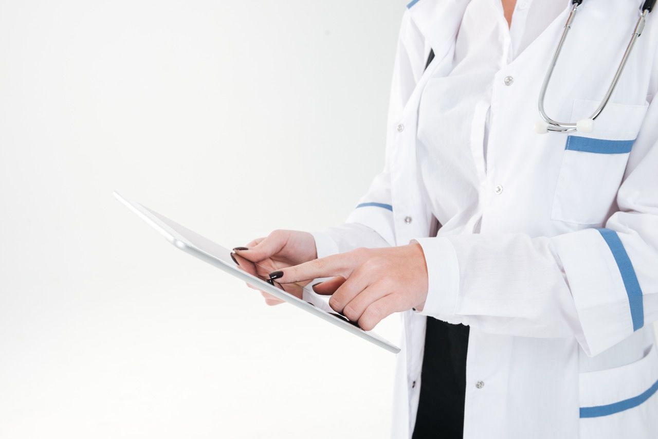 A female doctor in a white coat typing on a tablet.