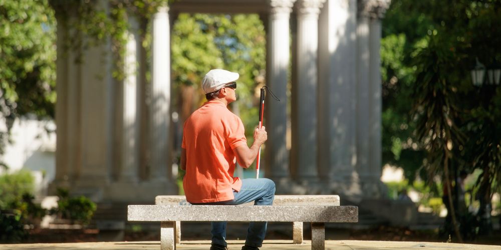 Blind man sitting in the sun on a park bench