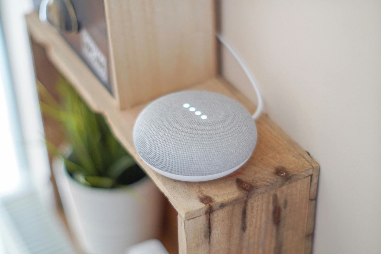 A grey Google Home speaker on a wooden shelf.