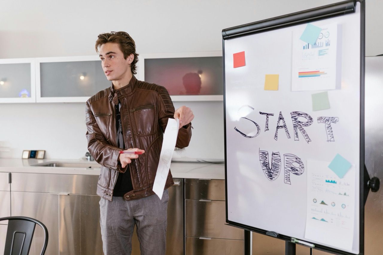 Young man in leather jacket presenting startup idea on a whiteboard.