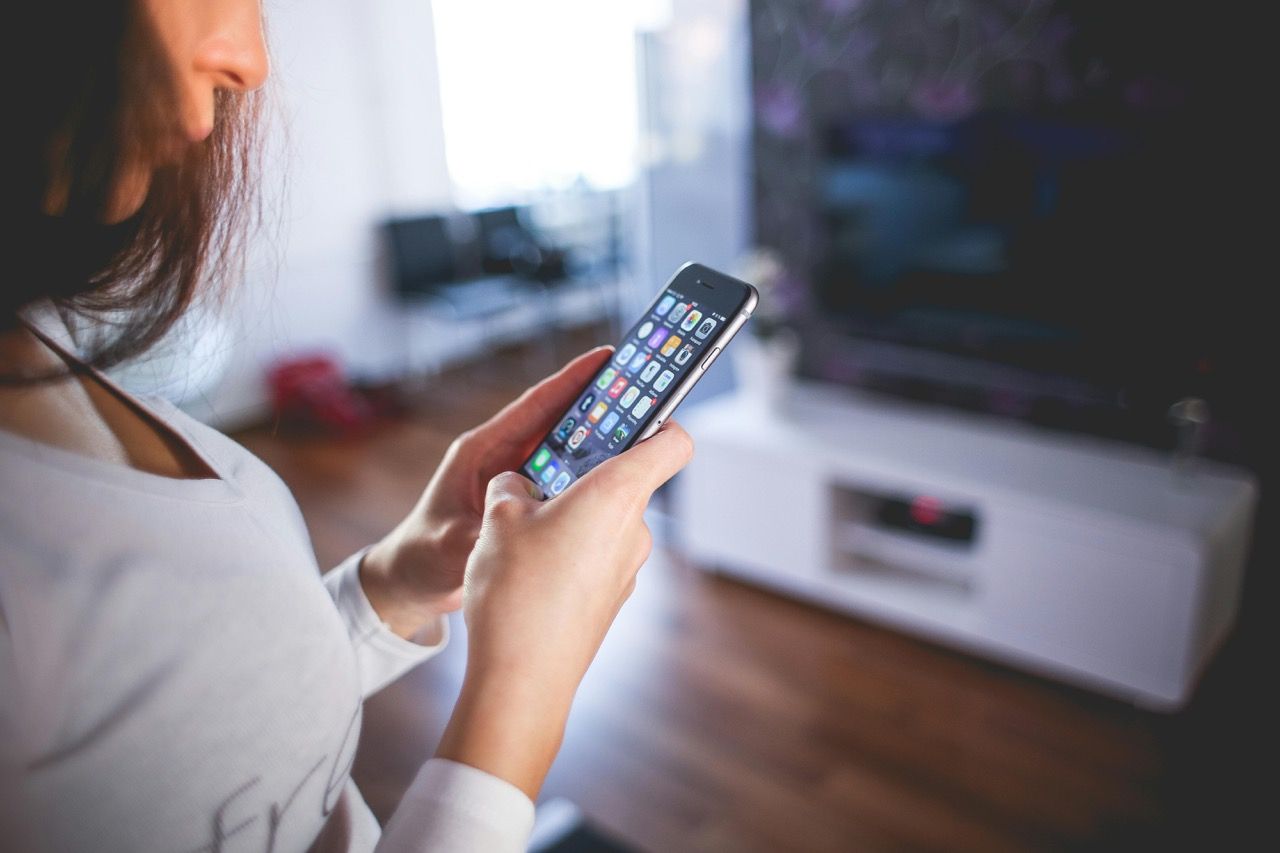 A woman is standing in front of a multimedia console with a flat-screen TV, holding a smartphone in both hands.