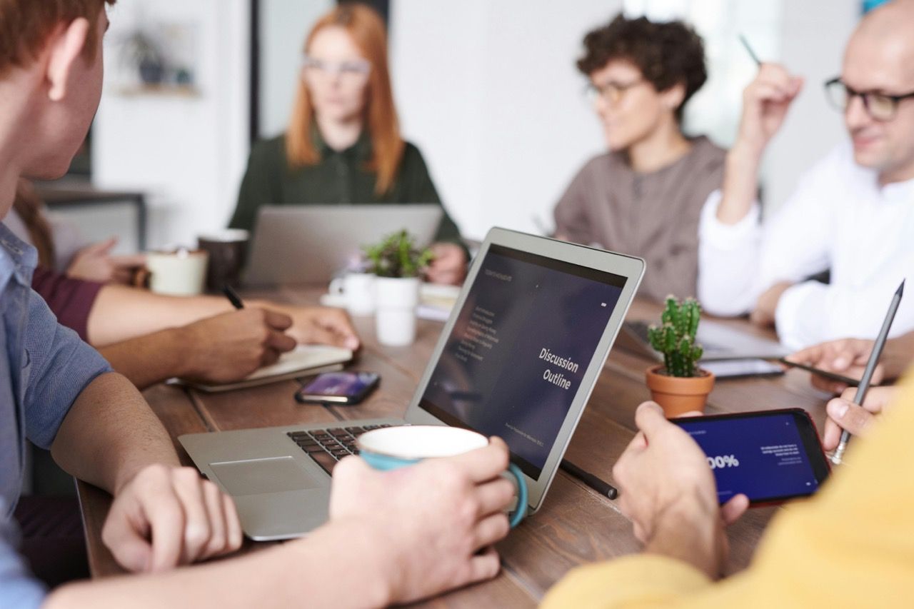 Eine Gruppe von Fachleuten arbeitet zusammen um einen Konferenztisch, mit Laptops, Kaffee und Notizen.